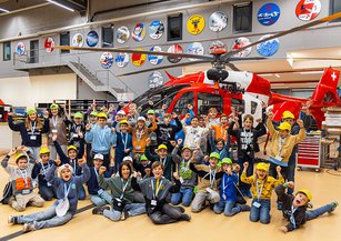 A group of children stand cheering in front of a rescue helicopter in the hangar.
