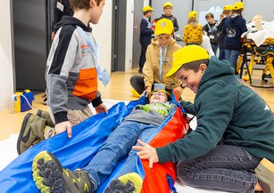 A group of children wrap a boy in a vacuum mattress.